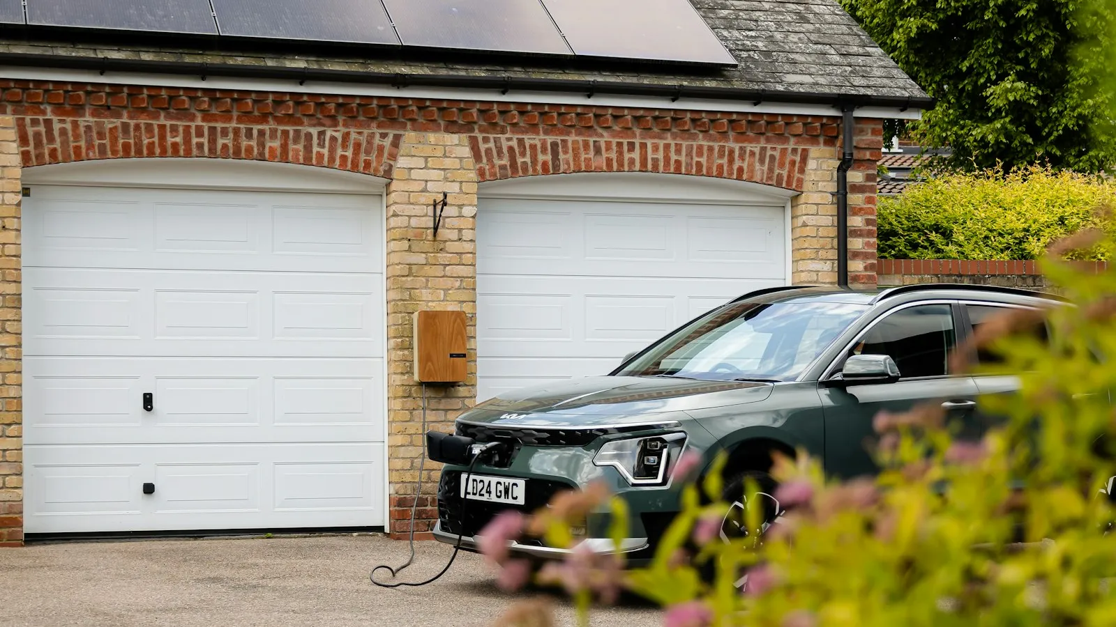 An EV charge point with its cable reaching a car parked on a driveway