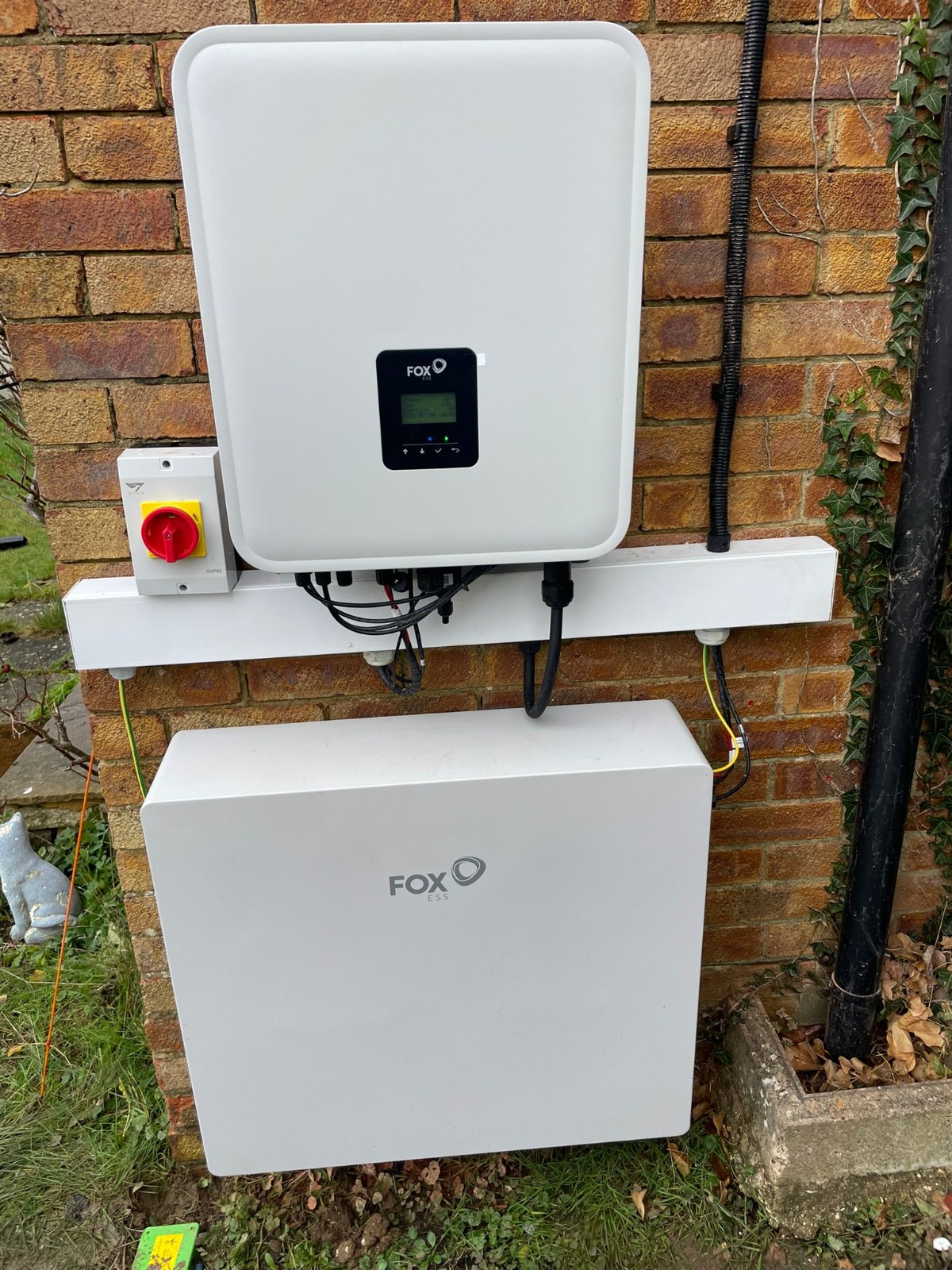 Battery and inverter mounted on the external brick wall of a home. Photographed by Cozy Home Solutions.