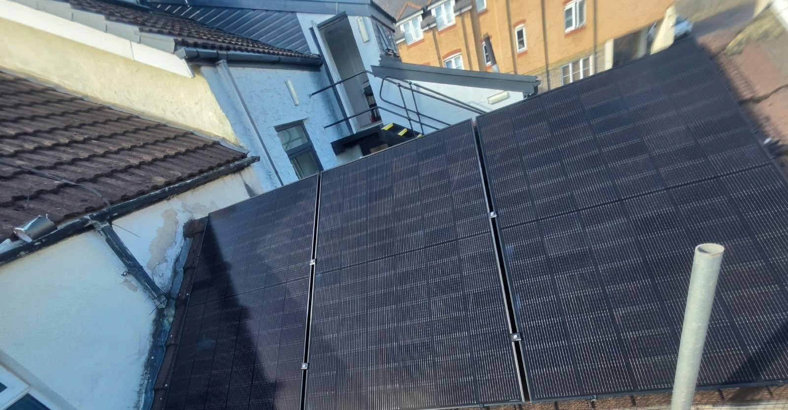 All-black solar panels photographed at roof level, with neighbouring homes behind, photographed by Cozy Home Solutions.