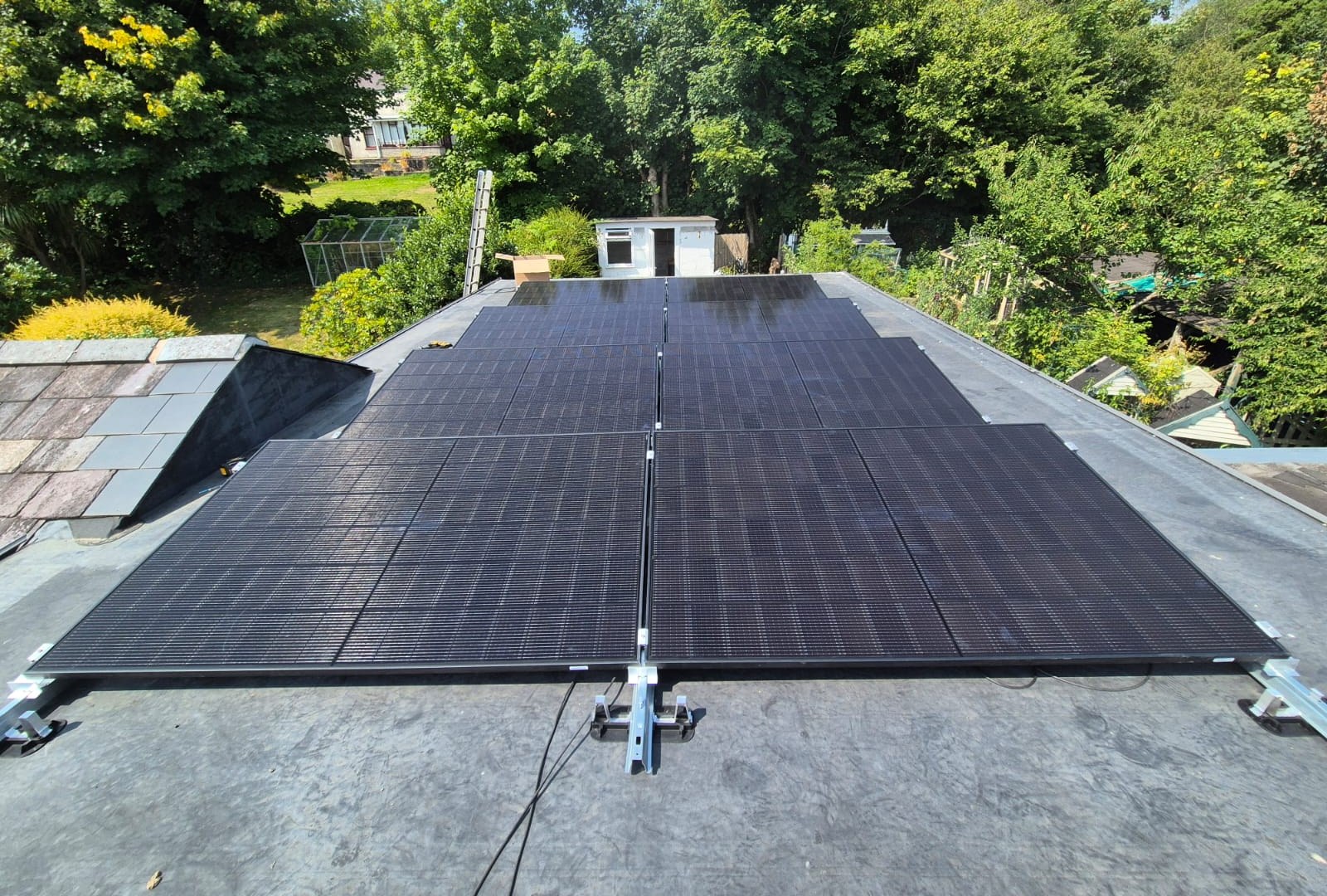 Eight all-black solar panels arranged in two rows on a flat rubber roof, angled towards the sky on a mounting frame.