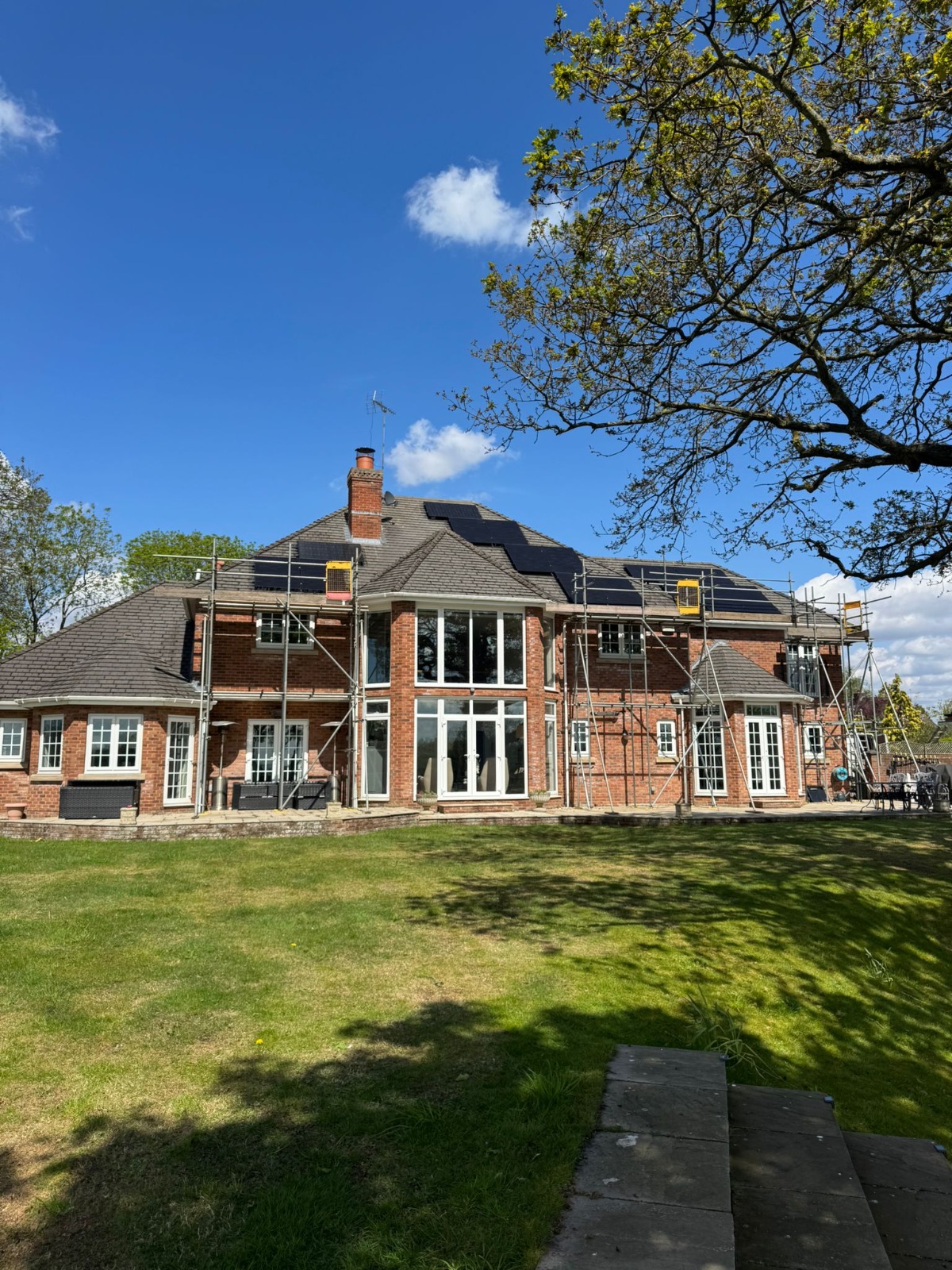 Solar panels being installed on the roof of a brick home in England, photographed by Cozy Home Solutions.