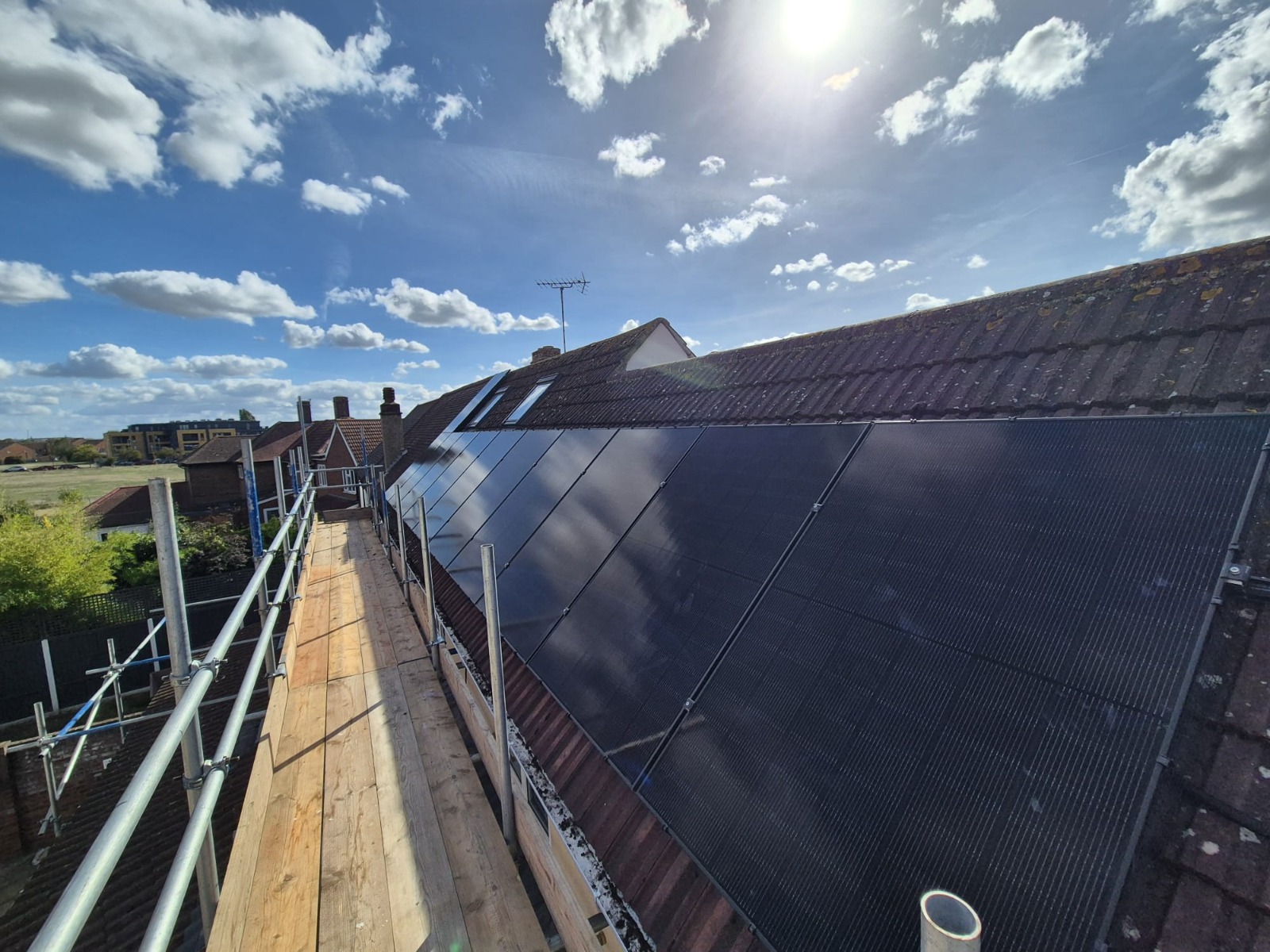 Rooftop solar panel array beside a scaffold walkway on a tiled pitched roof. Photographed by Cozy Home Solutions.